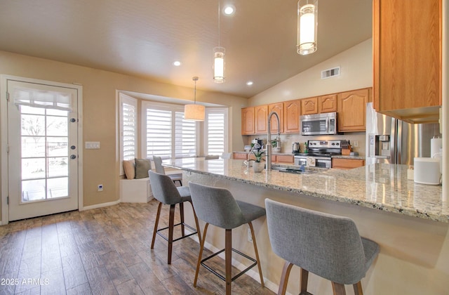 kitchen with wood finished floors, visible vents, appliances with stainless steel finishes, a kitchen bar, and decorative light fixtures