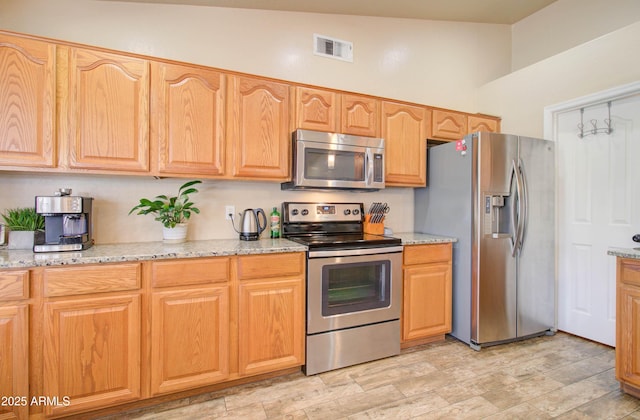 kitchen with light stone counters, visible vents, stainless steel appliances, and vaulted ceiling