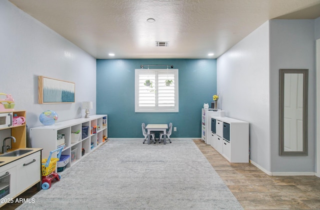 game room featuring baseboards, visible vents, a sink, a textured ceiling, and light wood-type flooring