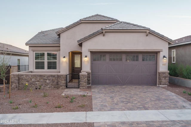 view of front of home featuring stone siding, an attached garage, fence, decorative driveway, and stucco siding