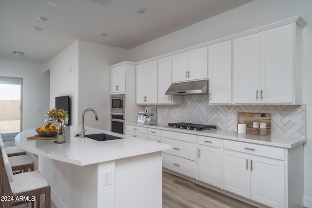 kitchen with stainless steel appliances, sink, white cabinets, light hardwood / wood-style floors, and an island with sink