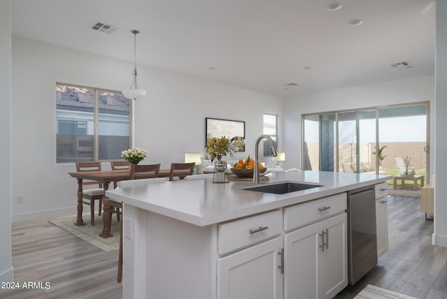 kitchen with sink, light hardwood / wood-style floors, white cabinetry, hanging light fixtures, and an island with sink