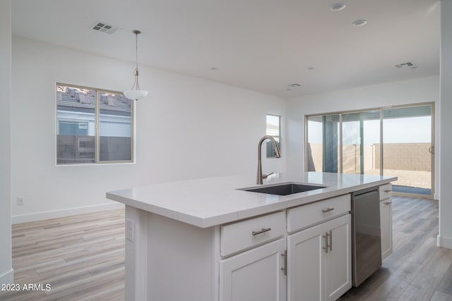 kitchen featuring light wood-type flooring, sink, decorative light fixtures, a center island with sink, and white cabinetry