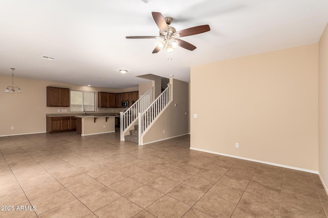 unfurnished living room with light tile patterned flooring, sink, and ceiling fan with notable chandelier