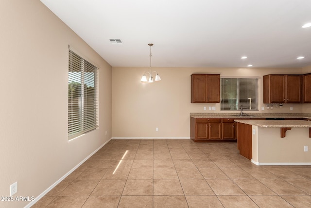 kitchen featuring pendant lighting, sink, a kitchen bar, a notable chandelier, and light tile patterned flooring