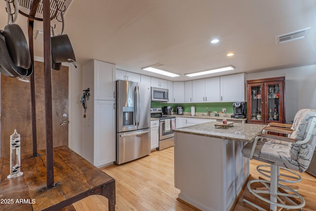 kitchen with visible vents, light wood-style floors, white cabinetry, appliances with stainless steel finishes, and a center island