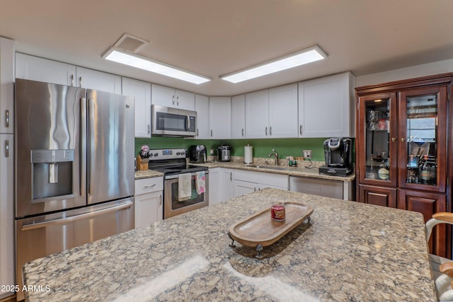 kitchen with light stone counters, stainless steel appliances, visible vents, white cabinetry, and a sink