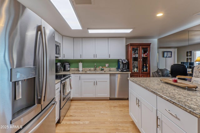 kitchen featuring stainless steel appliances, light wood finished floors, a sink, and white cabinetry