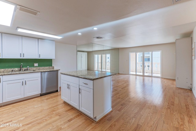 kitchen with dishwasher, light stone counters, open floor plan, and white cabinets