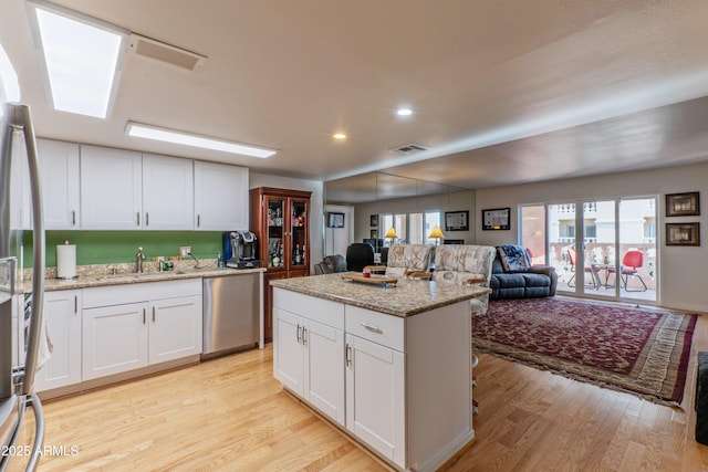 kitchen featuring stainless steel appliances, a sink, white cabinetry, open floor plan, and light wood finished floors