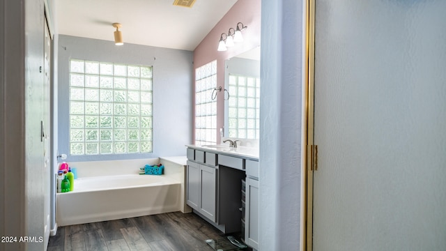 bathroom with a tub, vaulted ceiling, wood-type flooring, and vanity