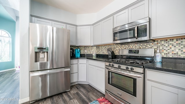 kitchen with appliances with stainless steel finishes, dark stone counters, dark wood-type flooring, and tasteful backsplash