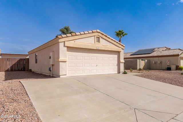 view of front of property with concrete driveway, a tile roof, fence, roof mounted solar panels, and stucco siding