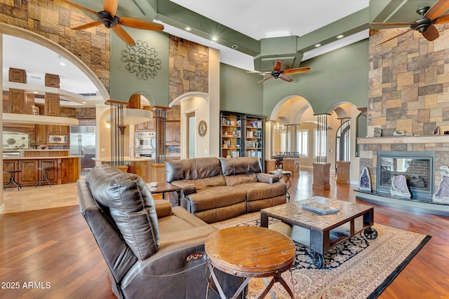 2371 E Sanoque Ct, Gilbert, AZ 85298 - living room featuring a ceiling fan, arched walkways, a towering ceiling, wood finished floors, and a stone fireplace
