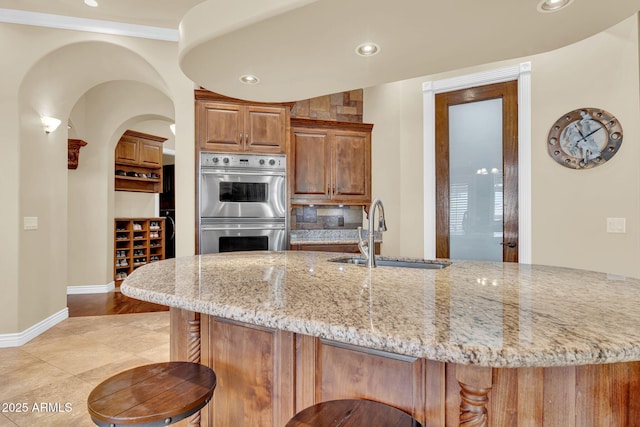 2371 E Sanoque Ct, Gilbert, AZ 85298 - kitchen with stainless steel double oven, light stone counters, a breakfast bar area, recessed lighting, and arched walkways