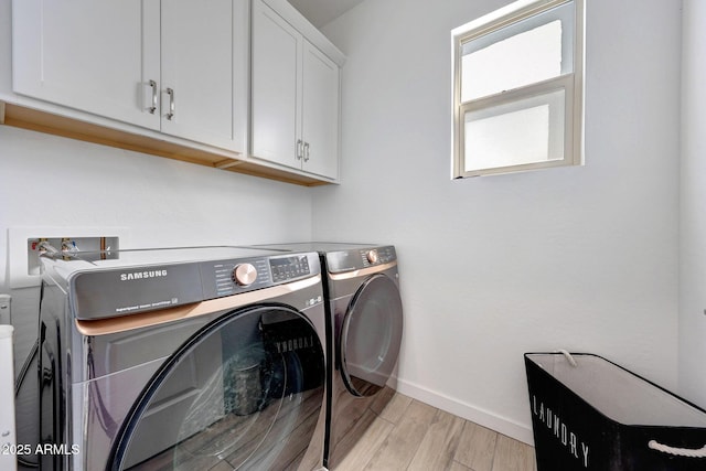 laundry area featuring light wood-type flooring, cabinet space, baseboards, and washing machine and clothes dryer