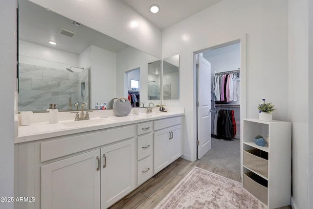 full bath with wood finished floors, double vanity, a sink, a shower stall, and a walk in closet