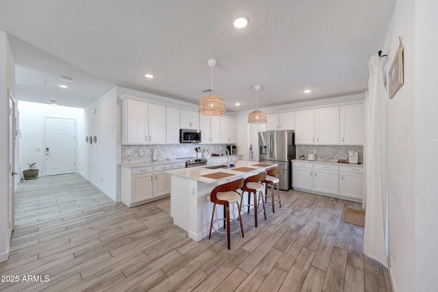 kitchen with backsplash, a breakfast bar area, light countertops, stainless steel appliances, and white cabinetry