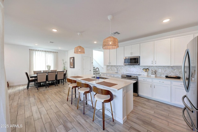 kitchen featuring visible vents, a sink, a kitchen breakfast bar, appliances with stainless steel finishes, and decorative backsplash