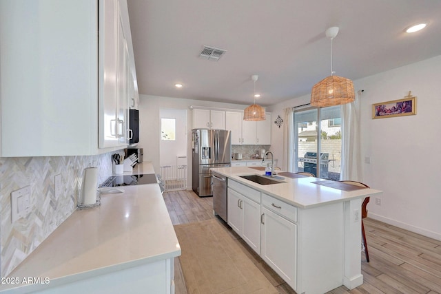 kitchen featuring light wood finished floors, visible vents, backsplash, stainless steel appliances, and a sink