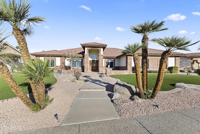 mediterranean / spanish-style home with brick siding, a tiled roof, a front lawn, and stucco siding