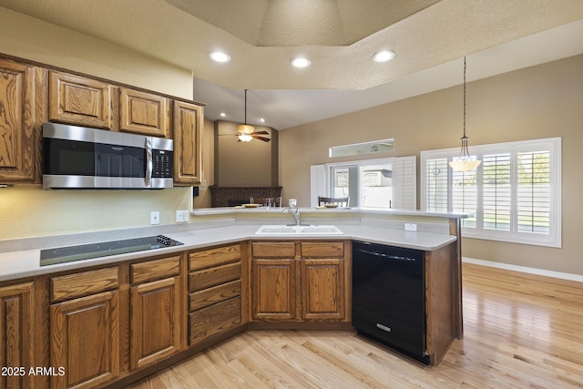 kitchen with a sink, light countertops, brown cabinets, black appliances, and decorative light fixtures