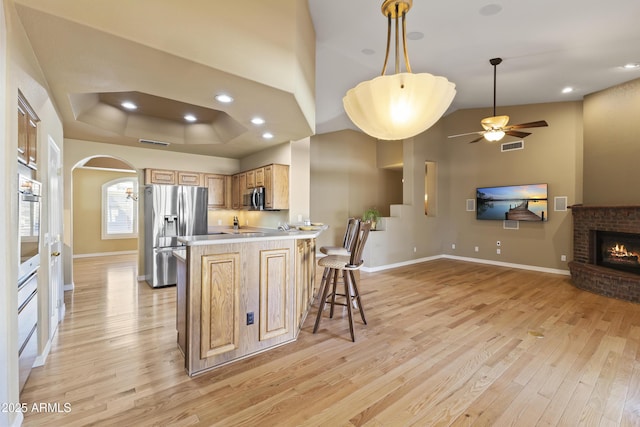 kitchen featuring stainless steel appliances, light countertops, light wood-style floors, open floor plan, and a peninsula