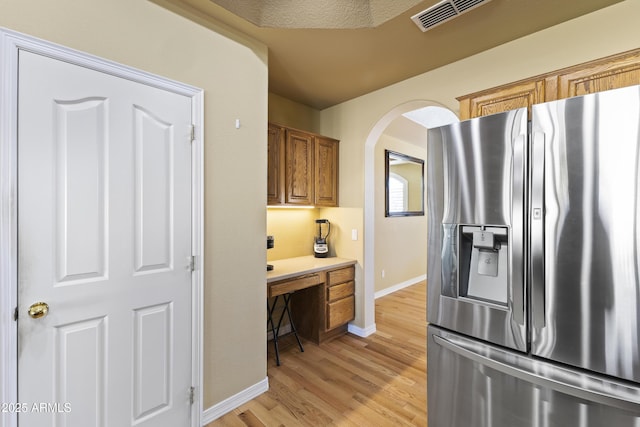 kitchen featuring visible vents, arched walkways, brown cabinets, light wood-style floors, and stainless steel refrigerator with ice dispenser