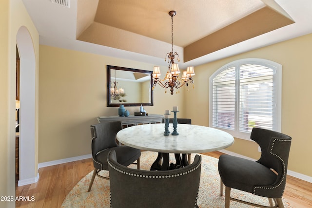 dining room featuring a tray ceiling, light wood-style flooring, and baseboards