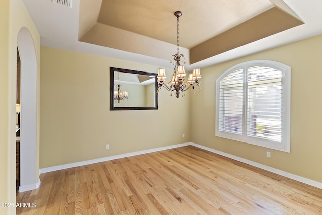 spare room featuring a tray ceiling, visible vents, an inviting chandelier, wood finished floors, and baseboards