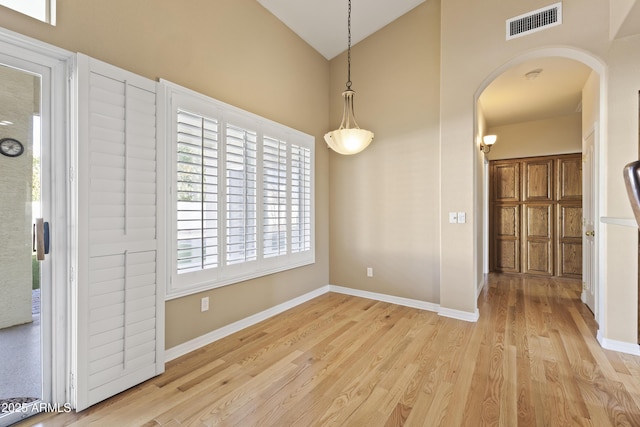 unfurnished dining area with arched walkways, light wood-style flooring, visible vents, and baseboards