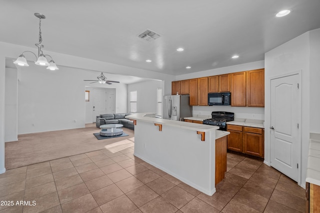 kitchen featuring ceiling fan with notable chandelier, pendant lighting, black appliances, light colored carpet, and a breakfast bar area