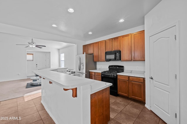 kitchen featuring a kitchen bar, ceiling fan, a kitchen island with sink, dark tile patterned flooring, and black appliances