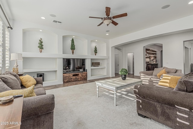 living room with built in shelves, arched walkways, a ceiling fan, recessed lighting, and carpet flooring