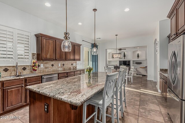 kitchen with appliances with stainless steel finishes, tasteful backsplash, a sink, a kitchen island, and light stone counters