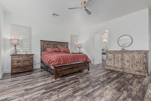 bedroom featuring arched walkways, dark wood-type flooring, baseboards, ceiling fan, and connected bathroom