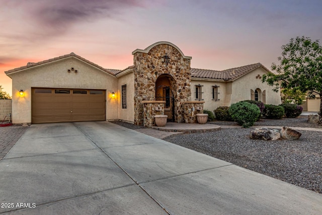 mediterranean / spanish-style home with concrete driveway, stucco siding, an attached garage, and stone siding