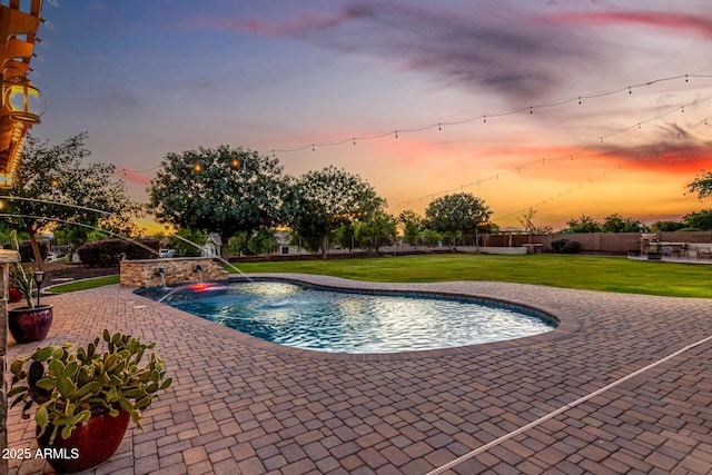 pool at dusk with a patio area and a lawn
