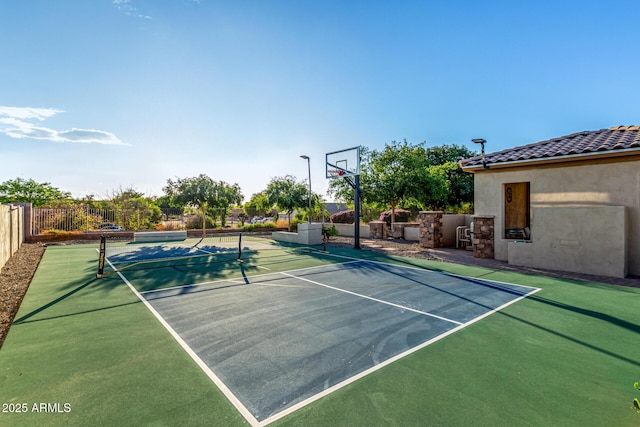 view of basketball court featuring a tennis court, fence, and basketball hoop