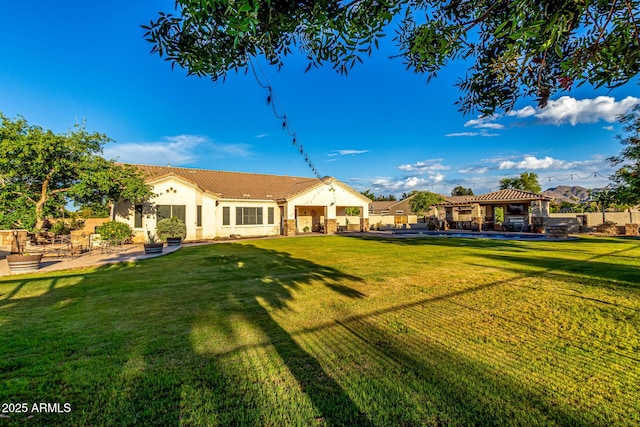 rear view of house featuring a gazebo, stucco siding, a patio, a lawn, and a tile roof