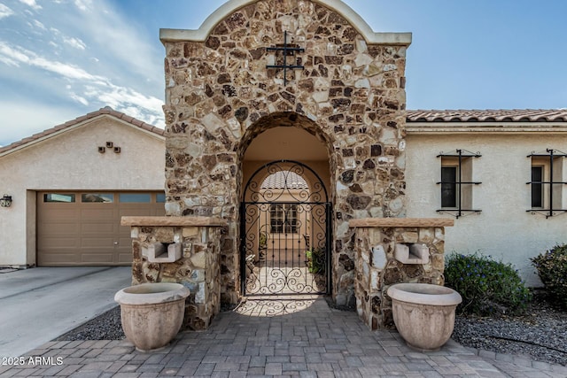 property entrance featuring concrete driveway, stucco siding, an attached garage, stone siding, and a tiled roof