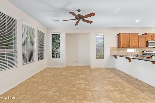 kitchen with ceiling fan, light tile floors, range, sink, and tasteful backsplash