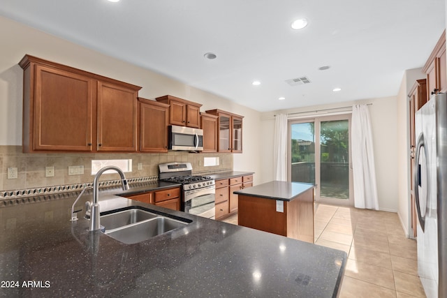 kitchen with backsplash, stainless steel appliances, dark stone counters, sink, and a center island