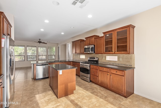 kitchen with appliances with stainless steel finishes, a center island, ceiling fan, light tile flooring, and tasteful backsplash