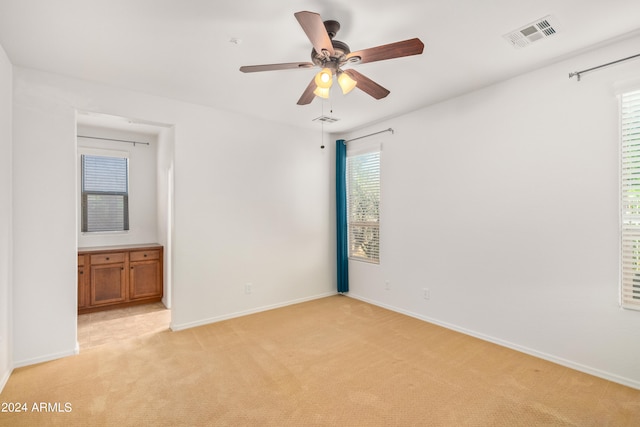 empty room featuring light colored carpet, ceiling fan, and a healthy amount of sunlight