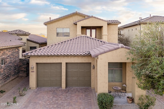 mediterranean / spanish home with a garage, a tile roof, decorative driveway, and stucco siding