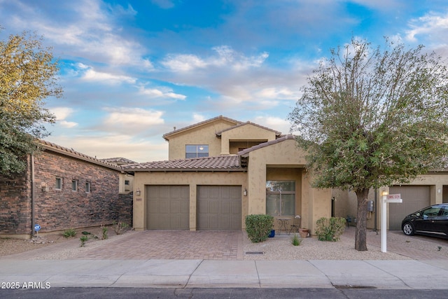 view of front of home featuring decorative driveway, a tile roof, an attached garage, and stucco siding