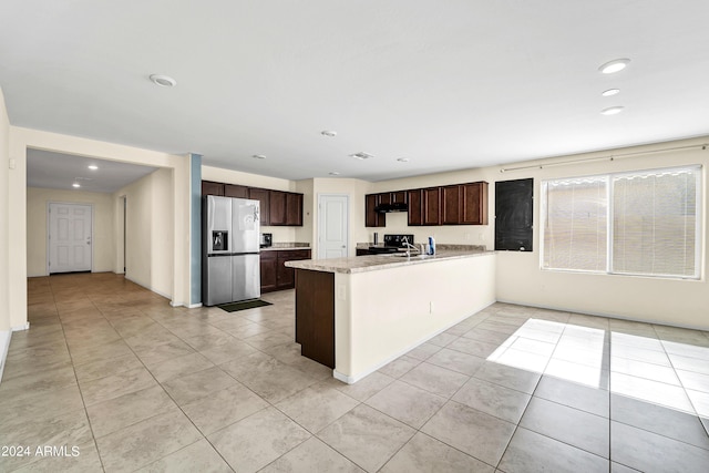 kitchen with light tile patterned floors, dark brown cabinets, stainless steel fridge, and kitchen peninsula