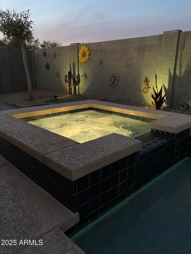 pool at dusk with an in ground hot tub