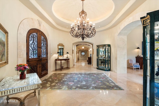 entryway with a tray ceiling, arched walkways, a notable chandelier, and marble finish floor